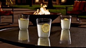 A photo of 3 glasses of lemonade on a patio table in front of a small backyard fire.
